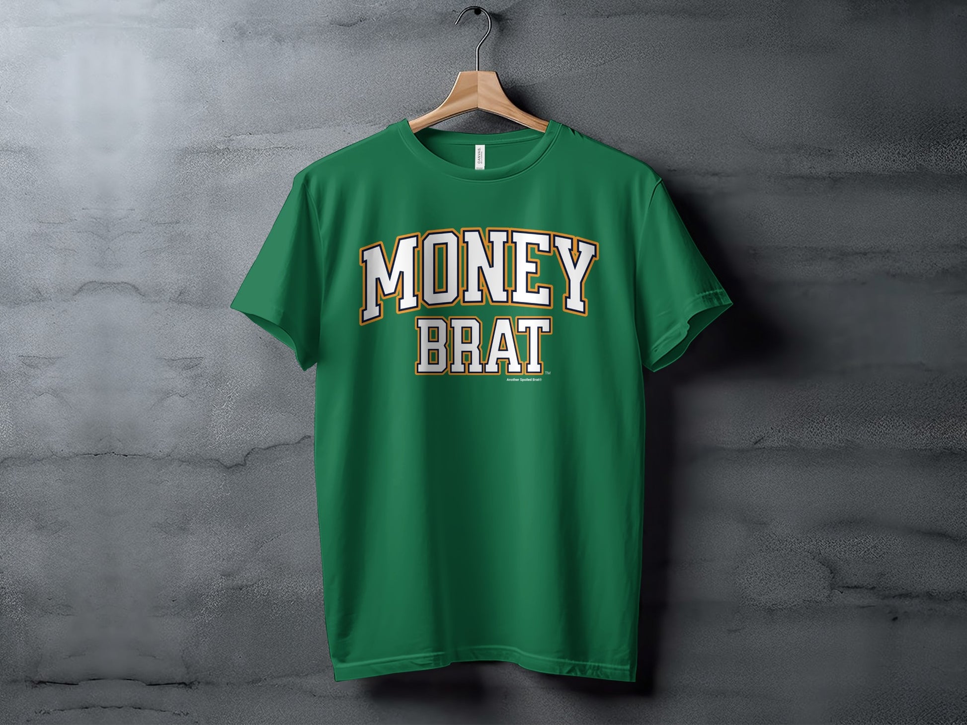 Green t-shirt with "MONEY BRAT" text, hanging on a wooden hanger against a textured wall.