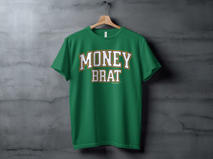 Green t-shirt with "MONEY BRAT" text, hanging on a wooden hanger against a textured wall.
