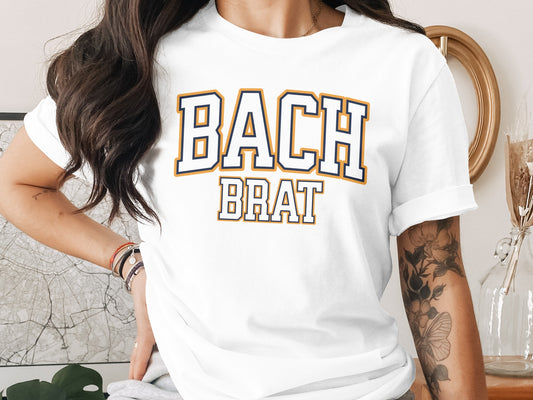 White t-shirt with "BACH BRAT" text in navy and orange collegiate font.