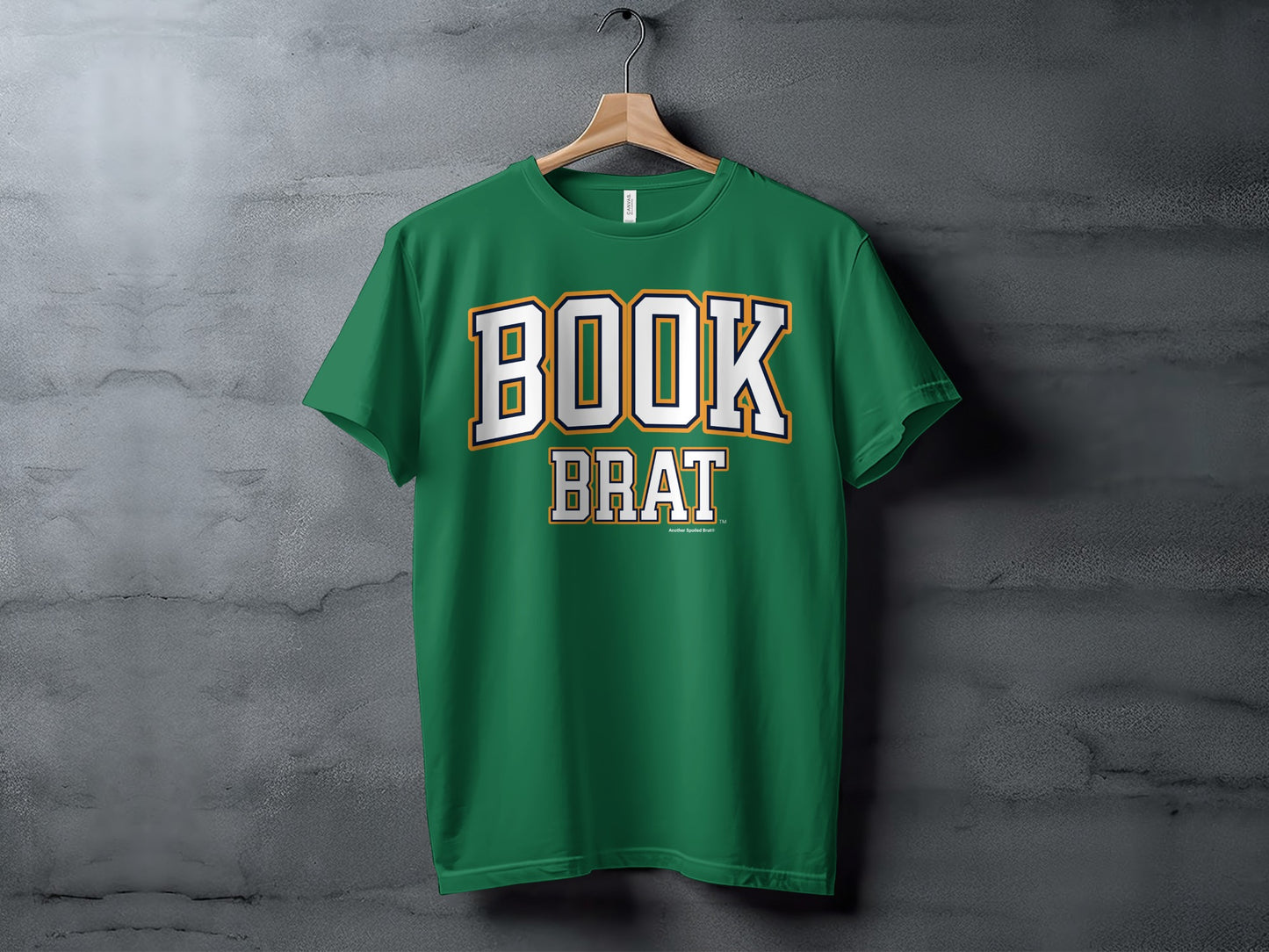 Green t-shirt with white and gold "BOOK BRAT" text, hanging on a hanger.