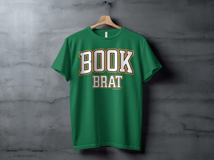 Green t-shirt with white and gold "BOOK BRAT" text, hanging on a hanger.