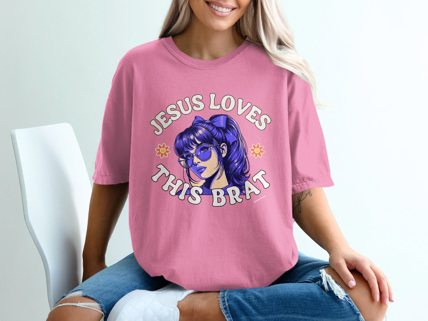 Pink t-shirt with "Jesus Loves This Brat" text and cartoon sunglasses.
