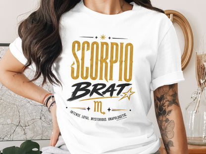 White t-shirt with "SCORPIO BRAT" text, Scorpio symbol, and descriptive words.