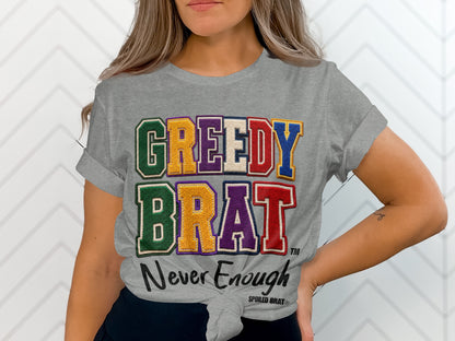 Grey t-shirt with "GREEDY BRAT Never Enough" text in colorful, appliquéd letters.