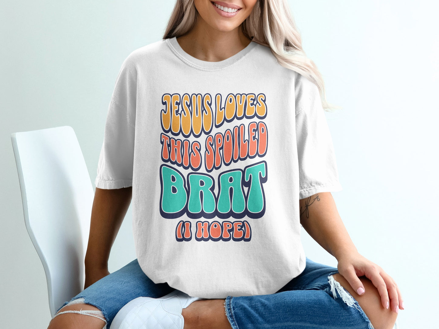 White t-shirt with "Jesus Loves This Spoiled Brat (I Hope)" text in retro lettering.