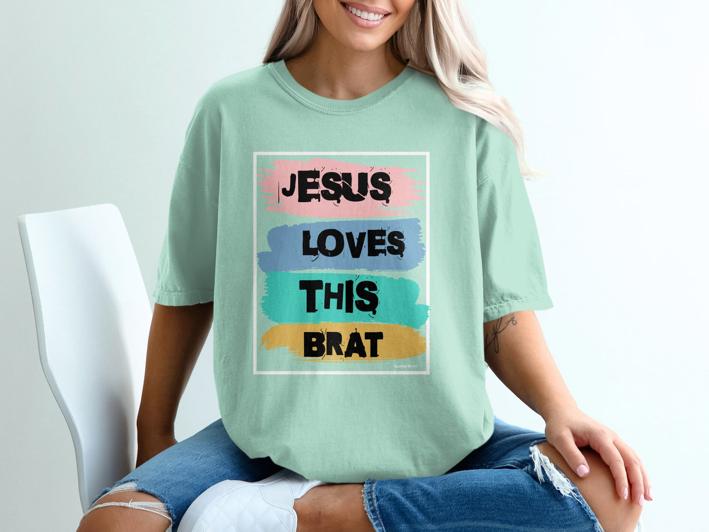Light mint t-shirt with distressed text "Jesus Loves This Brat" in pink, blue, and green.