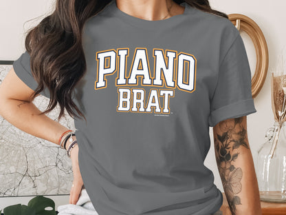 Gray t-shirt with white and orange "PIANO BRAT" text