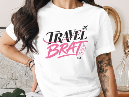 White t-shirt with black and pink "TRAVEL BRAT" text and airplane design.