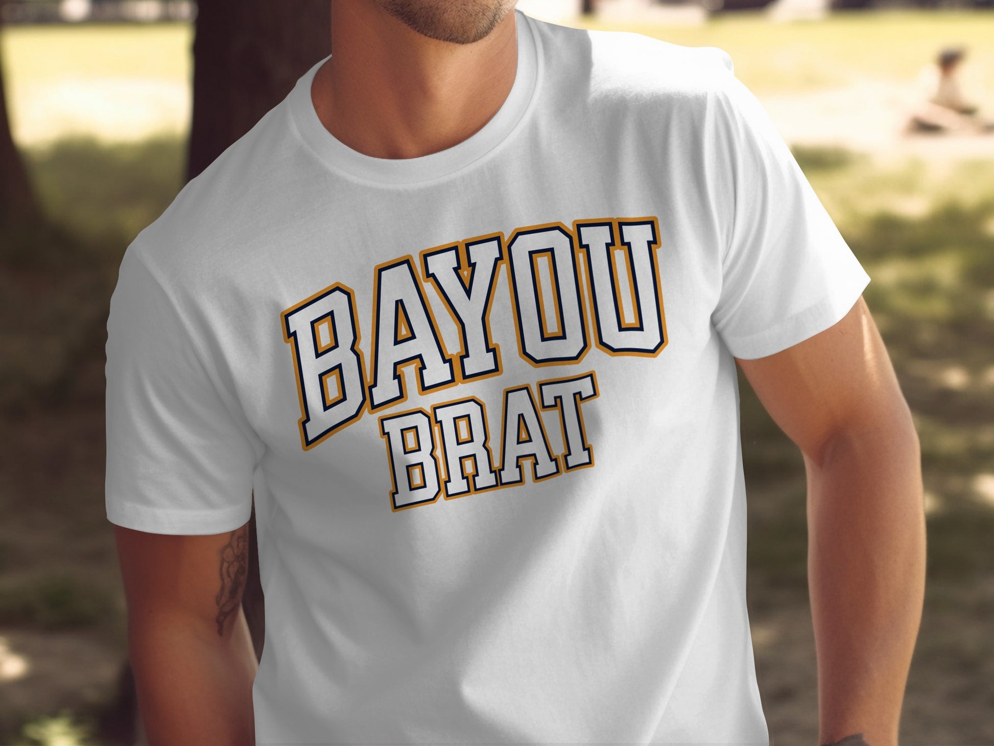 White t-shirt with "BAYOU BRAT" written in bold navy and gold letters.