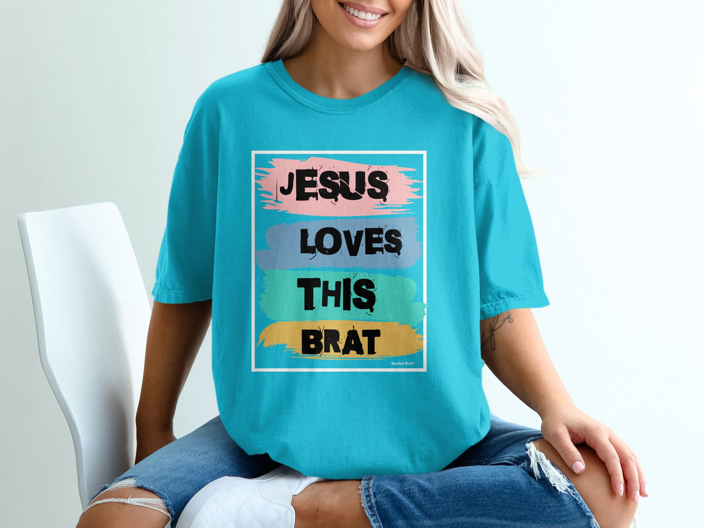 Teal t-shirt with "Jesus Loves This Brat" text in colorful brush strokes.
