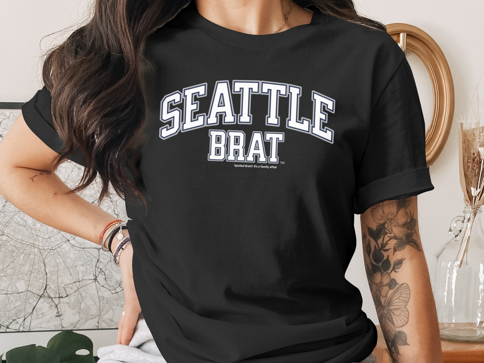 Black t-shirt with white "SEATTLE BRAT" text and a family affiliation tagline.