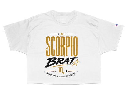 White cropped t-shirt with "SCORPIO BRAT" and zodiac symbols in gold and black.