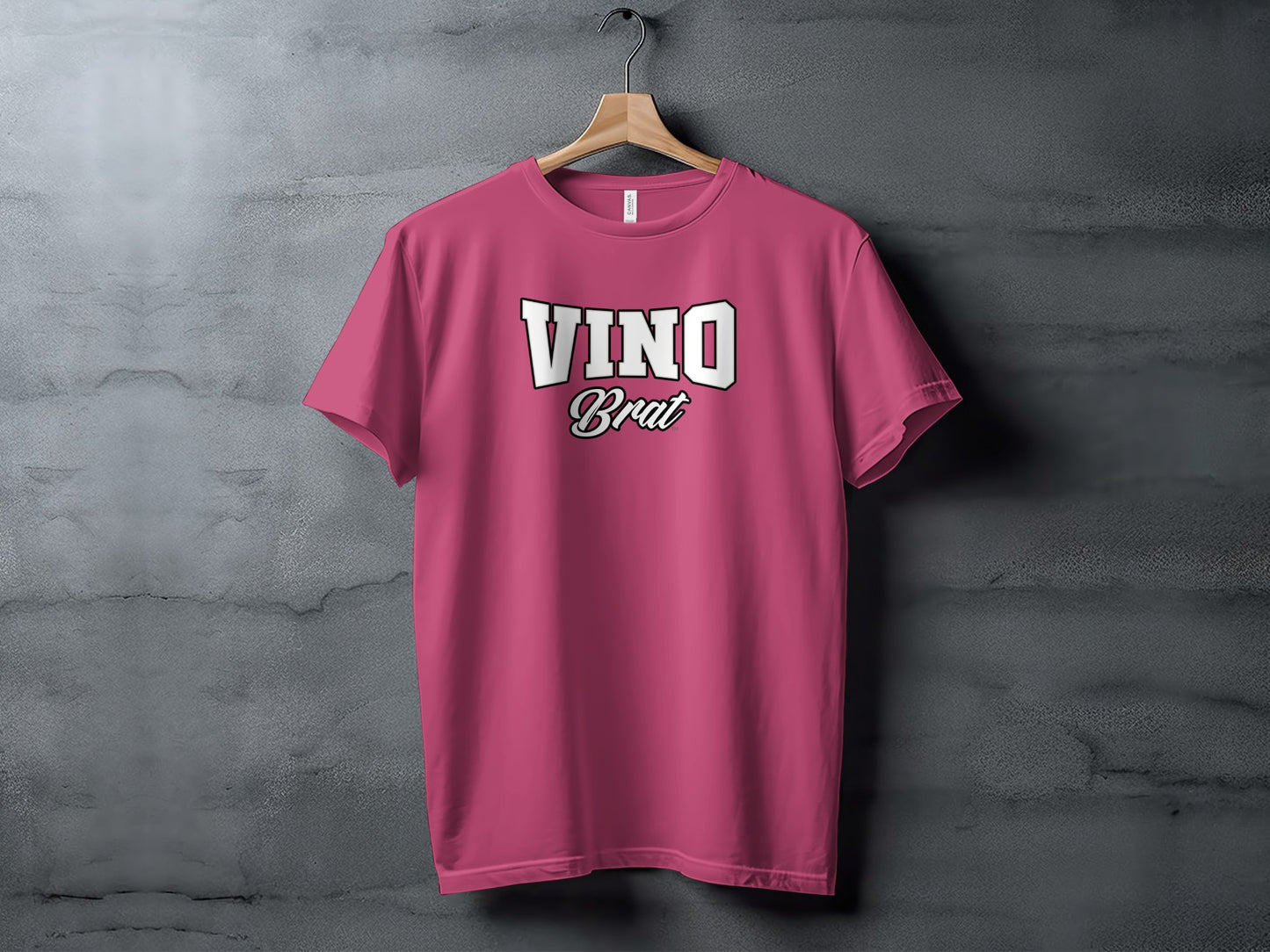 Pink t-shirt with white "VINO Brat" text hanging on a wall.
