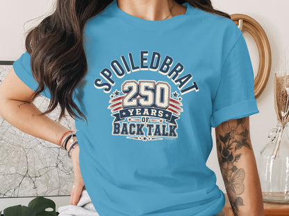 Blue t-shirt with "Spoiledbrat 250 years of back talk" graphic.