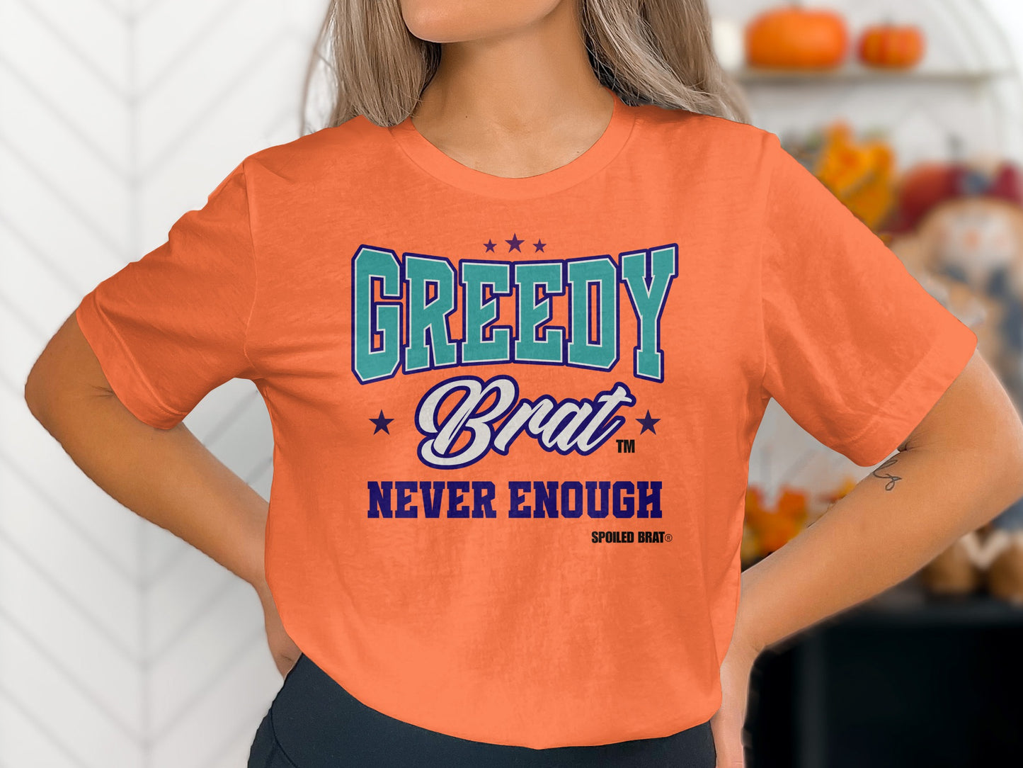 Orange t-shirt with "GREEDY Brat NEVER ENOUGH SPOILED BRAT®" text.